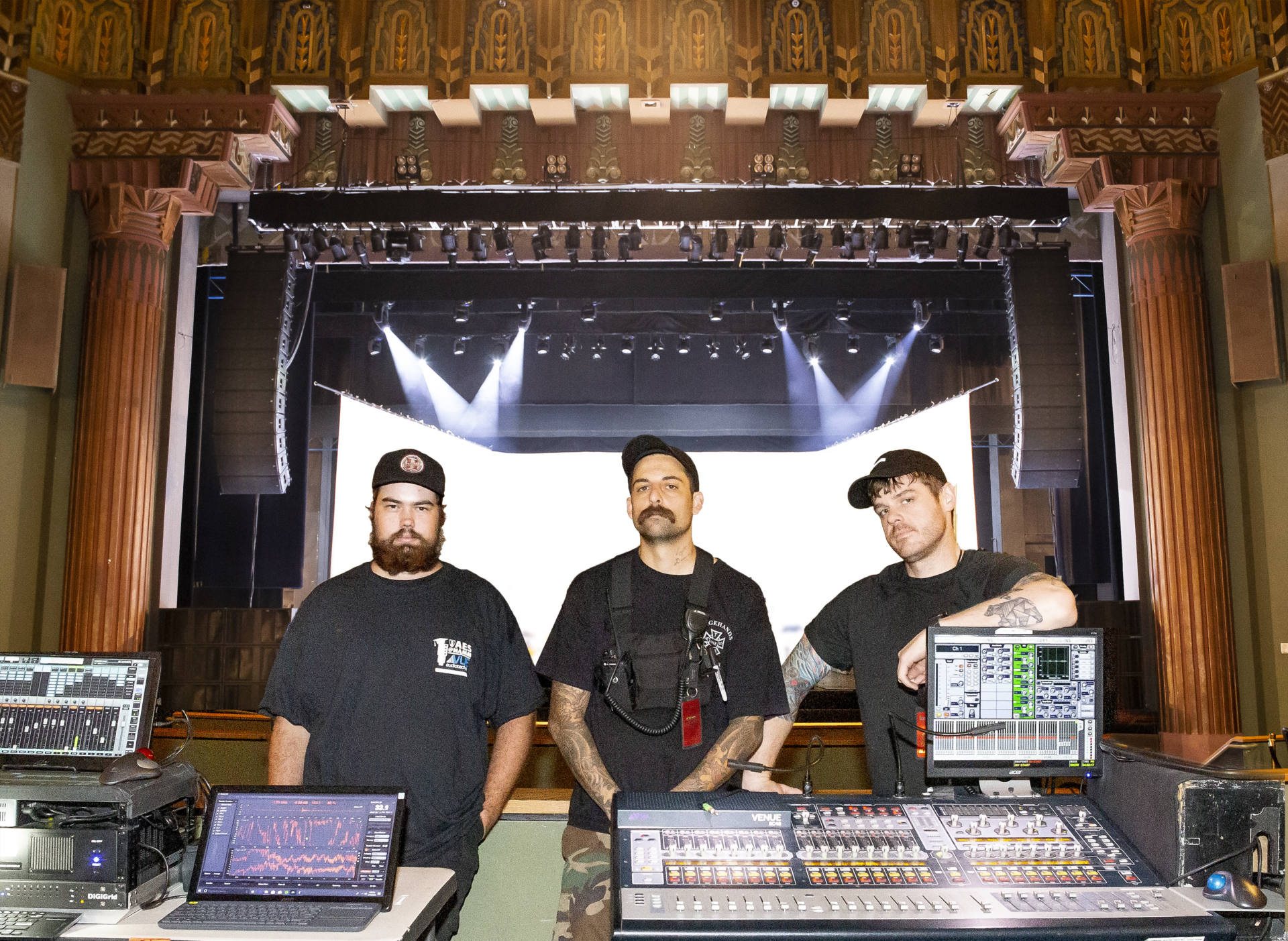 Three men stand behind audio equipment at a historic venue